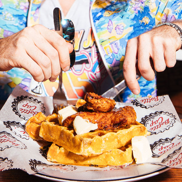 A person cutting into chicken and waffles at Bottle Cap Nashville