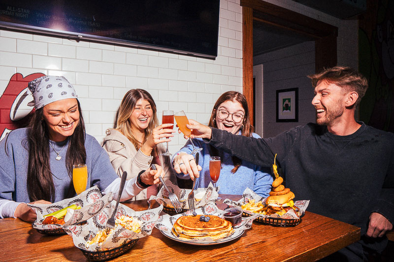 A group of young people eating, laughing, and drinking at Bottle Cap