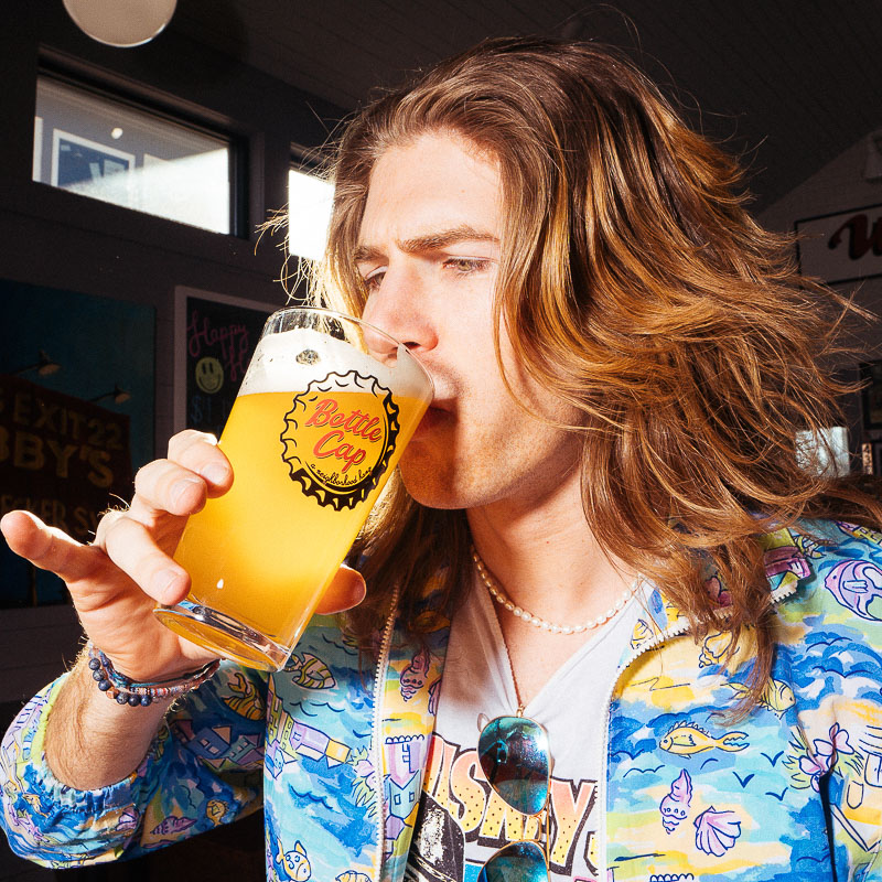 A man drinking beer from a Bottle Cap glass with one pinky finger raised up